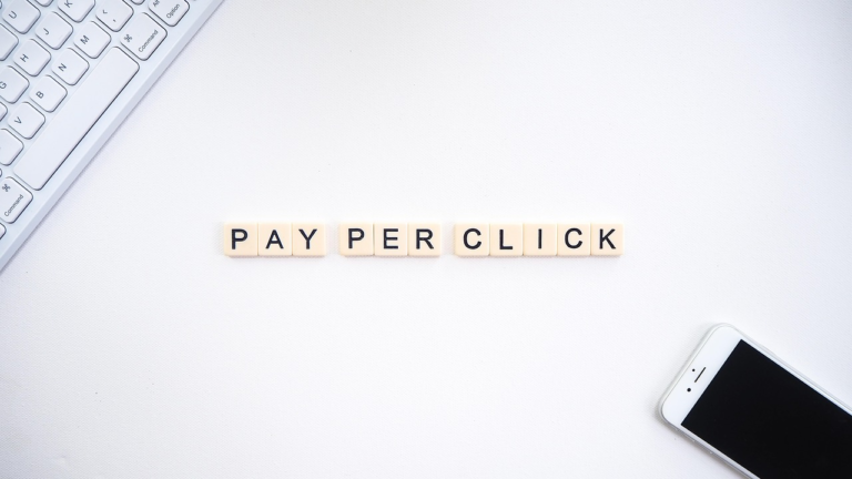 Pay per click (PPC) advertising concept with scrabble letters on a white desk next to a keyboard and smartphone.